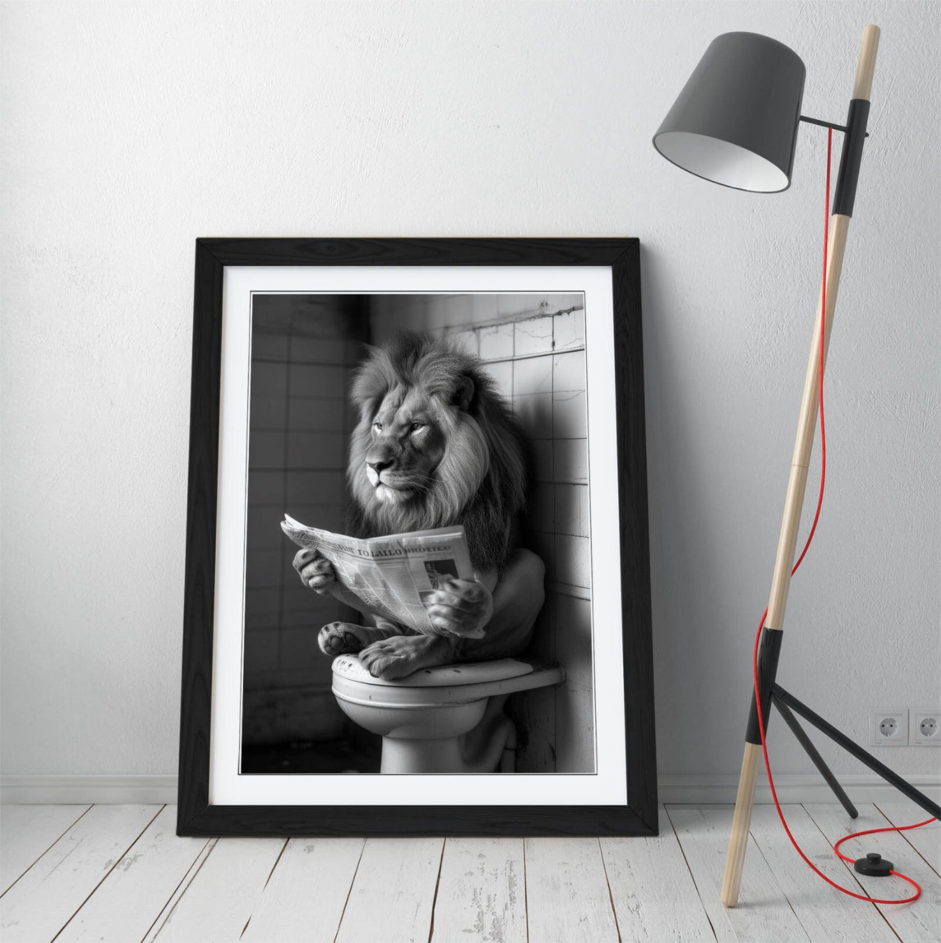 Framed black and white print of a lion reading a newspaper on a toilet, leaning against a tiled wall.